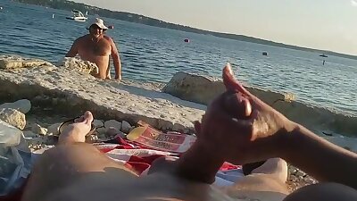 On a nude beach the wife stokes my cock while a voyuer watches